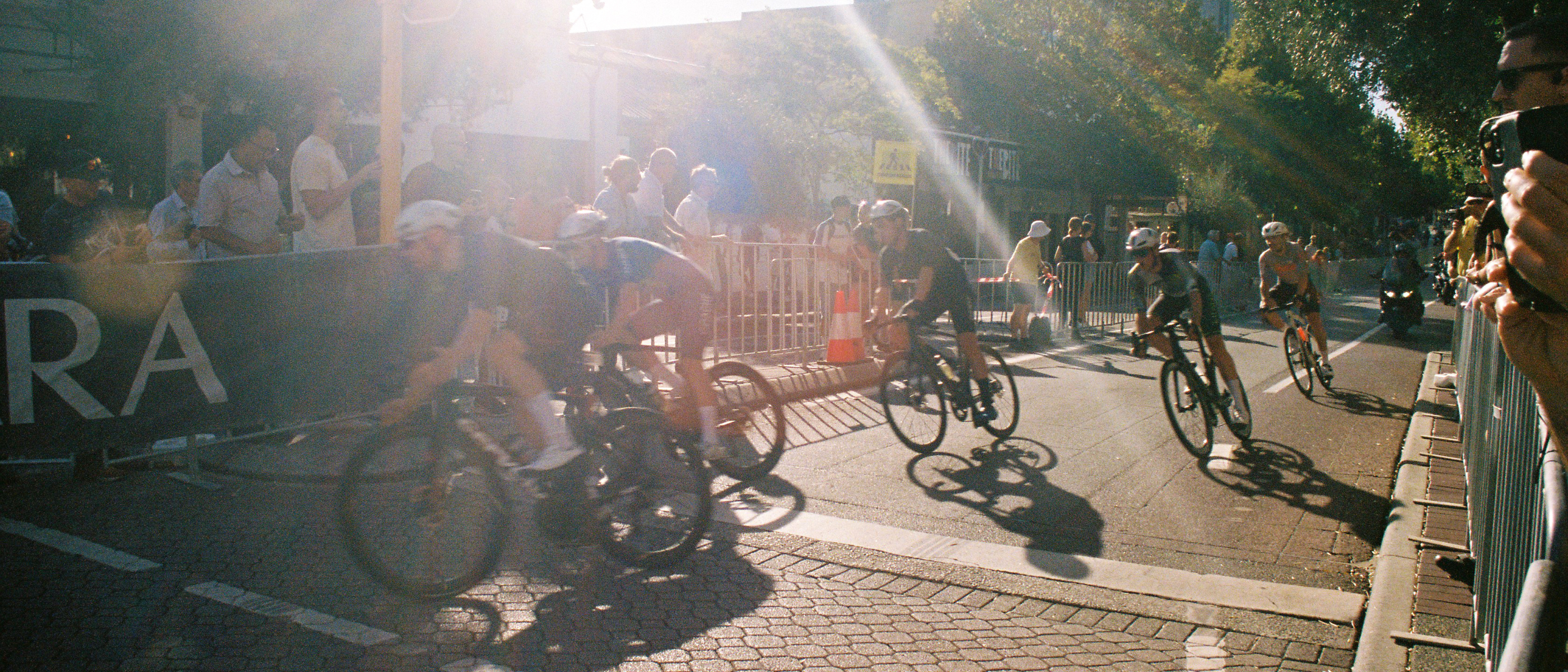 A film style photo of road cyclists racing through a street.
