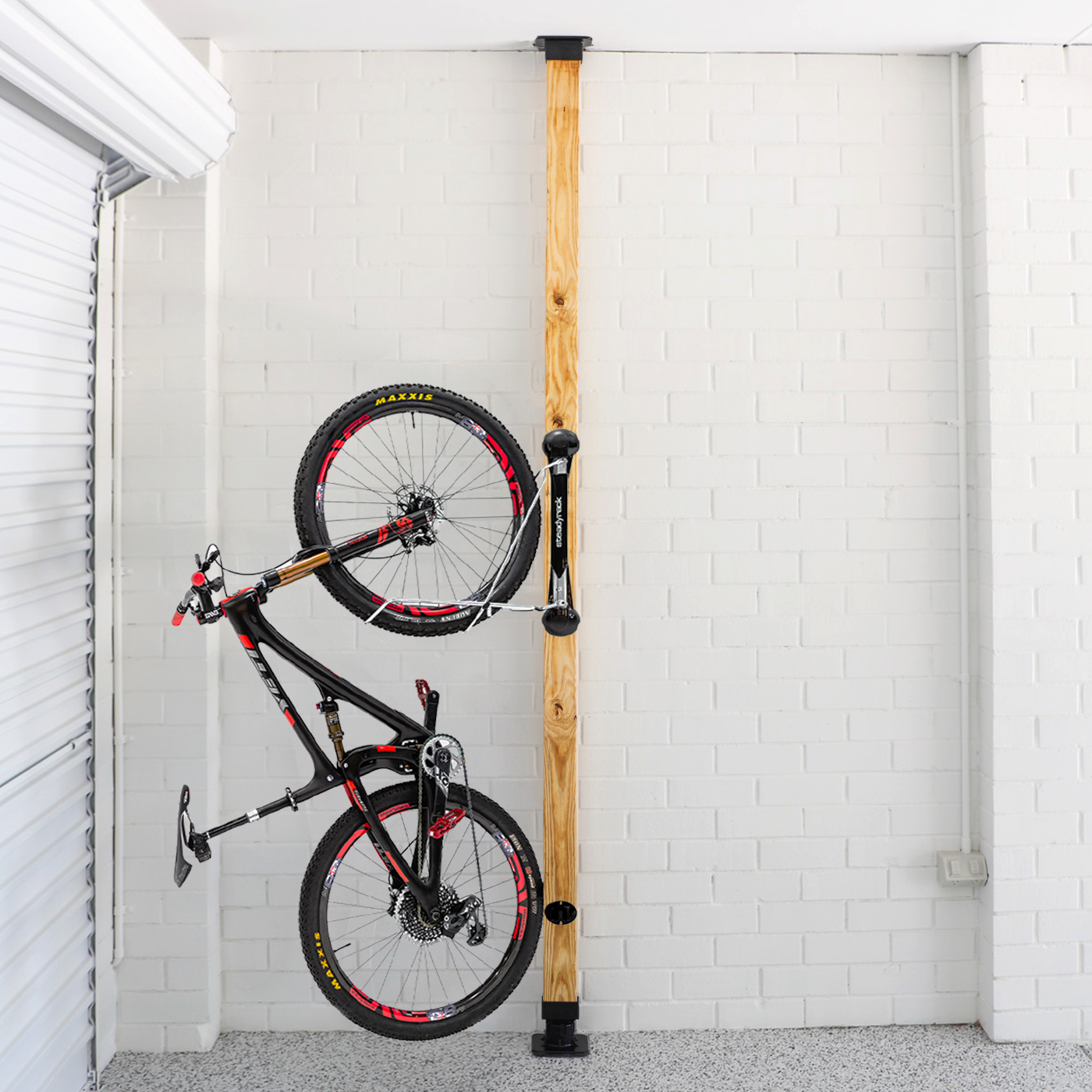 Bicycle mounted against a wooden post with white brick walls.